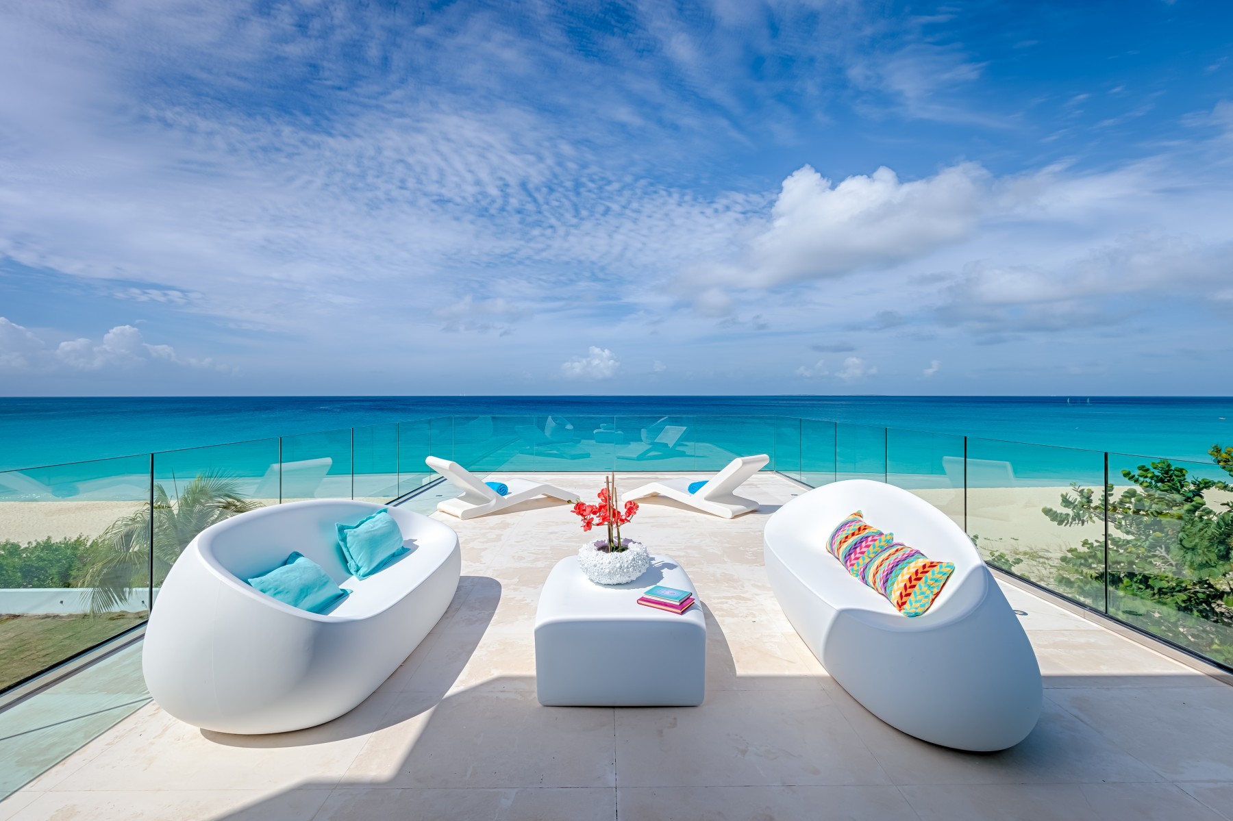 Modern terrace with stylish white furniture overlooking an endless ocean view, featuring a unique oval table and chic lounging chairs under a clear blue sky in Anguilla