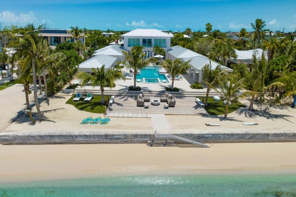 Aerial view of a luxurious beachfront villa with a large pool and palm trees in Turks and Caicos
