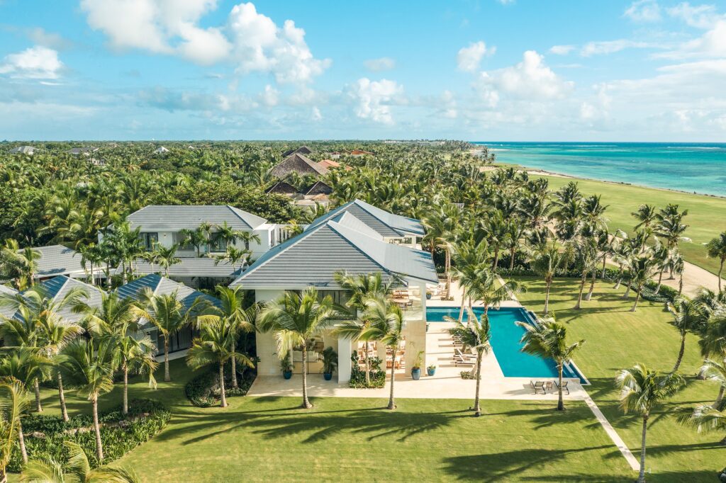 Aerial shot of a sprawling luxury villa complex surrounded by lush greenery and adjacent to a sandy beach in the Caribbean, perfect for high-end vacations and retreats in Punta Cana