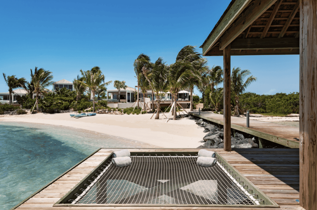 Beachfront villa with palm trees and a hammock net over the water in Turks and Caicos