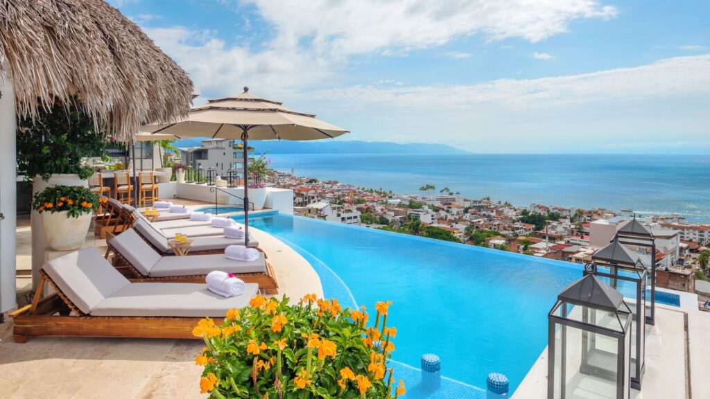 Infinity pool with white loungers and umbrellas, overlooking a coastal city and blue ocean with mountains in the background in Puerto Vallarta