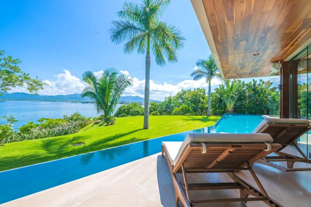 Infinity pool with wooden loungers overlooking a lush garden and the ocean in Punta Mita