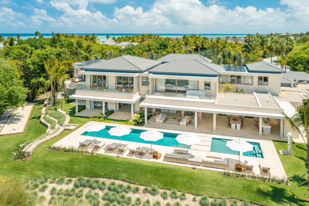 Aerial view of a grand beachfront luxury villa in the Caribbean with multiple swimming pools, lush gardens, and direct beach access, showcasing a perfect vacation retreat in Punta Cana