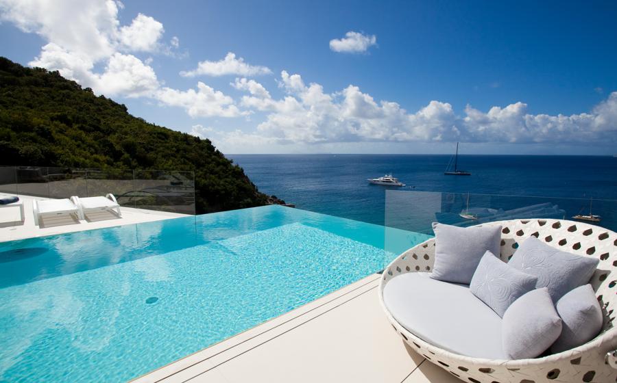 Luxurious infinity pool overlooking the Caribbean Sea with a white yacht sailing in the distance, surrounded by lush tropical greenery in St Barts