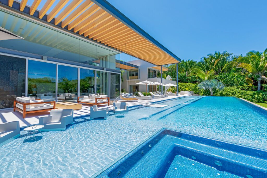 Modern poolside area with white loungers, seating, and a hot tub, adjacent to a contemporary villa in Punta Mita