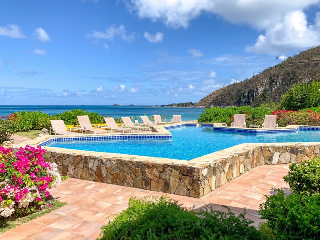 Luxury resort-style pool with a natural stone border, surrounded by vibrant flowering shrubs and ocean views, offering a tranquil and picturesque setting for relaxation in Virgin Gorda
