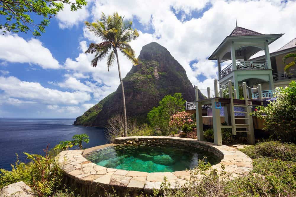Beautiful stone hot tub with a palm tree, ocean, and mountain in the background in St Lucia