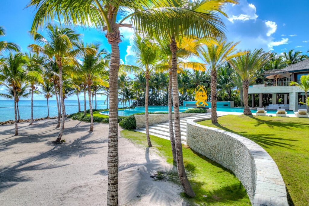 Stunning tropical villa pathway lined with palm trees leading to a turquoise swimming pool and a spacious patio area, highlighting exclusive privacy and scenic beauty in Punta Cana
